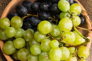 Green and black grapes in a wooden plate