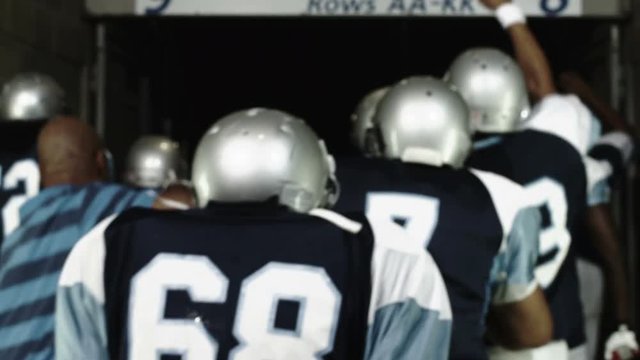 A hyped-up football team walks away from the camera down a tunnel