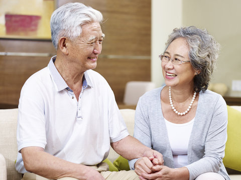 happy senior asian couple sitting on couch chatting