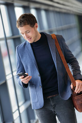 Man on smart phone - young business man texting in airport. Casual urban professional businessman...