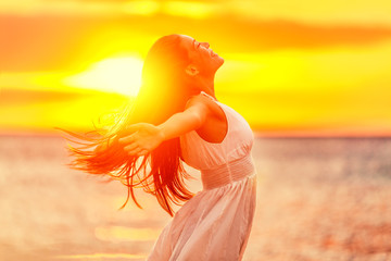 Happy woman feeling free with open arms in sunshine at beach sunset. Freedom and carefree enjoyment...