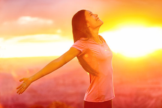 Happy people - carefree woman enjoying free nature at sunset. Freedom, serenity, wellness and spirituality concept - Asian girl with open arms in ecstatic enjoyment praising life to the sky.