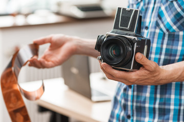 Photographer standing with retro medium format camera and negative film. Unrecognizable man holding...
