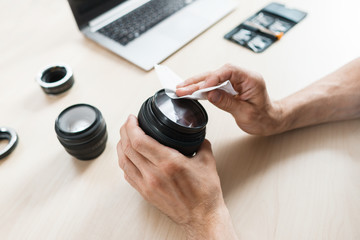 Camera lens cleaning with wet wipe, close-up. Photographer hands wiping lens on workplace . Professional photographing equipment care, technology, hobby concept