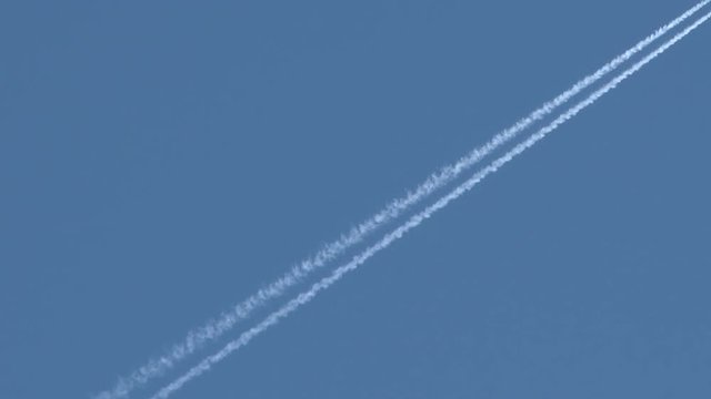 Airplane flies overhead through frame on clear, blue sky day leaving behind vapor trail jet contrails.