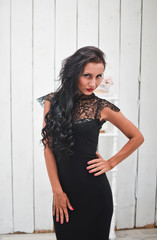 Girl in black dress posing against white wooden wall.