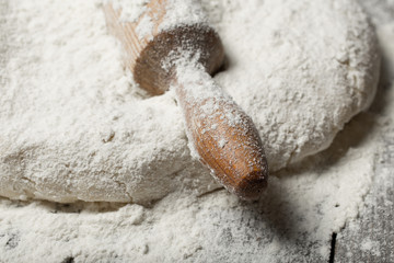 Rolling pin with flour on wooden table in bakery