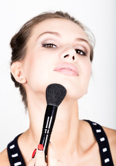 Close-up Female model applying makeup on her face. Beautiful young woman applying foundation on her face with a make up brush.