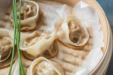 High angled view of cooked dumplings inside bamboo steamer with lip partially off.