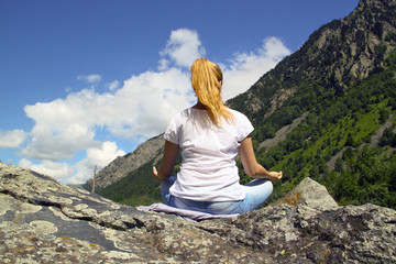 Naklejka premium Young woman meditating on top of a mountain in the wilderness
