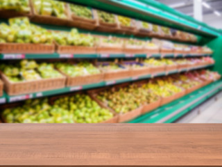 Wooden empty table in front of blurred supermarket fruits and vegetables shelf