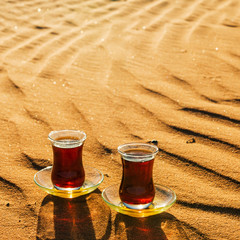 Black tea in traditional glasses and pot on desert