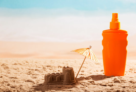 Sunscreen, sand castle and umbrella on seashore.