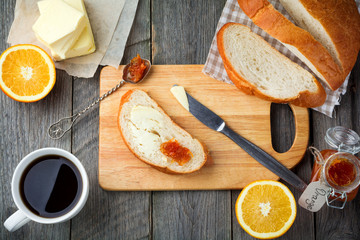 Ingredients for breakfast. Bread, butter, orange marmalade and a cup of tea with a wooden board in the center of the old wooden background. Selective focus.Top view. Copy space.