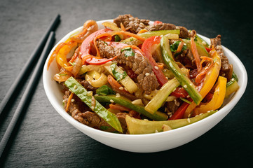 Asian (korean) salad with beef, vegetables and sesame seeds on black board.