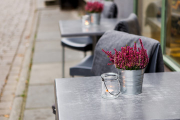 Cafe tables stand on the street. On the chairs are warm plaids. On the tables there are flowers and candles. The old European street. Autumn cloudy.