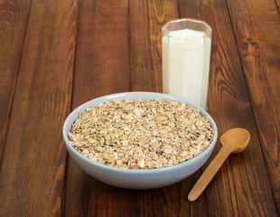 Bowl oatmeal, glass milk and spoon on background dark wood.
