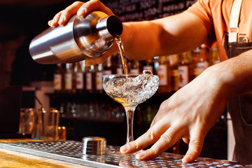 Männlicher Barkeeper macht Cocktail-Shaker mit gießendem Alkohol