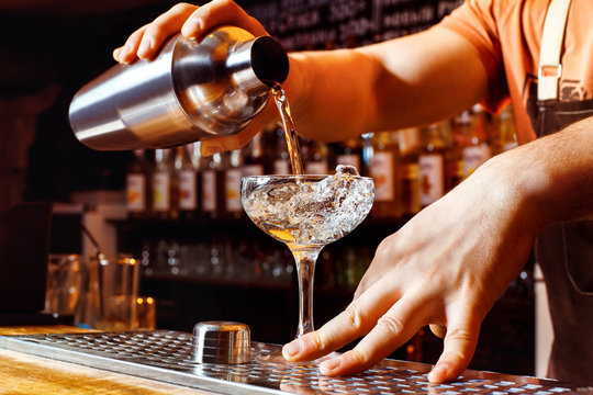 Male bartender is making cocktail holding shaker with pouring alcohol