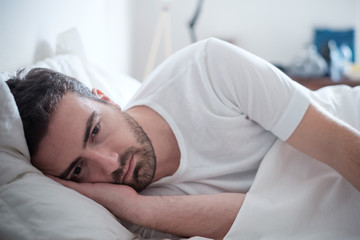 Depressed man lying in his bed and feeling bad - obrazy, fototapety, plakaty