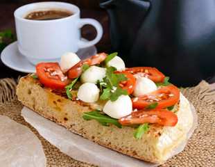 Classic sandwich with mozzarella, fresh tomatoes, arugula and sesame seeds on toast and a cup of coffee. Breakfast.