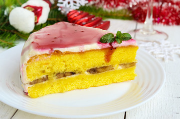 Sponge cake with a layer of banana, milk cream and cranberry syrup on a white background. Holiday dessert. Christmas theme. 