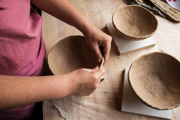 Girl in a pink apron sculpts bowls of pottery clay in pottery workshop © Olha Kozachenko