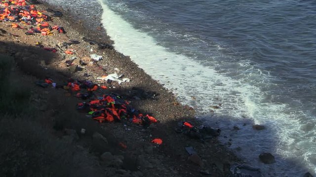 LESVOS, GREECE - NOV 2, 2015: Abandoned by the refugees belongings and life jackets on the rocky shore.