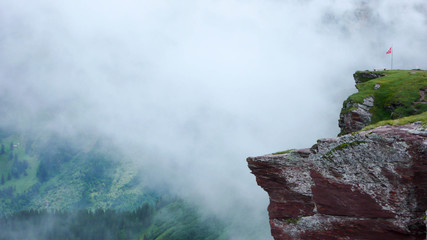 standing on the edge of a mountain cliff after a rain storm with clouds and the Swiss flag in the Swiss Alps near Flums