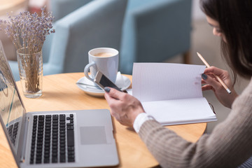 Close up of young woman making notes and using laptop.