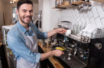 Joyful handsome waiter using coffee machine.