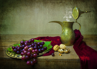 Still life with fresh bunch of grapes placed in vintage tray with walnuts,silky scarf and old copper pot on rustic wooden table. © dinasaeed