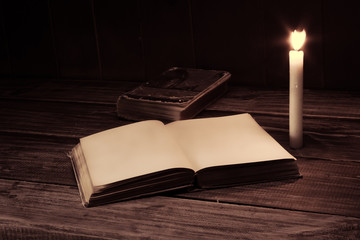 old antique opened book with burning candle near on the wooden table. Blank page
