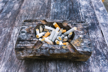 Cigarette butts with ash in ashtray on grey wooden table