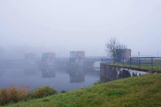 Old water dam on the river in the morning mist. Autumn fog over the river weir. 