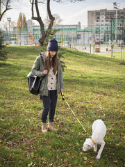 Young woman playing with a white boxer dog in the park.