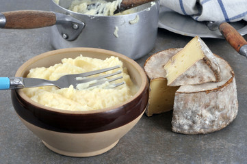 Un bol d'aligot à côté d'un morceau de tomme de savoie