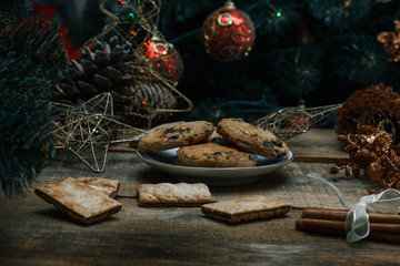 Beautiful concept. Chocolate cookies on a white plate on a wooden background. Nearby stands a Christmas tree, toys, garlands and Christmas toys.