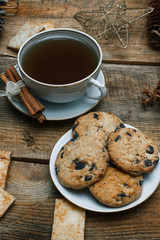 Beautiful concept. Chocolate cookies on a white plate on a wooden background and tea. Nearby stands a Christmas tree, toys, garlands and Christmas toys.