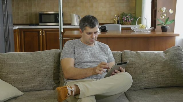 Male 40 - 45 years sitting on the couch with digital tablet