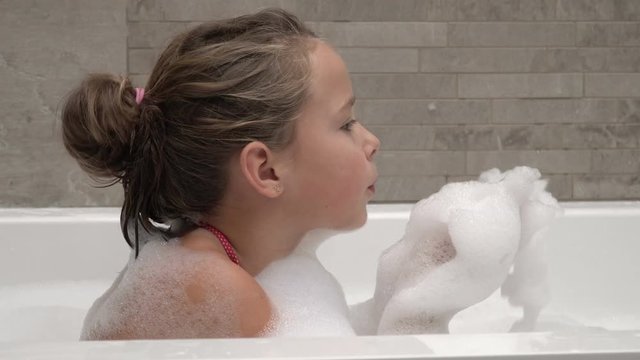 Little girl playing in the bathroom, blowing on the foam