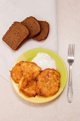 Potato pancakes with meat and sour cream on green plate with rye