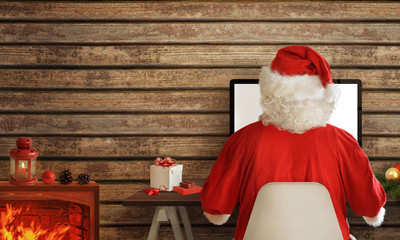 Santa Claus shopping online on computer from his warm room. In addition to the fireplace with fire,...