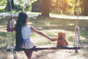 Little Girl play with Teddy bear sitting on a swing.