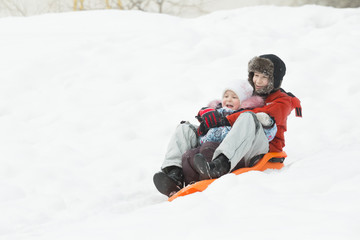 Happy siblings having downhill fun on winter orange plastic snow slider