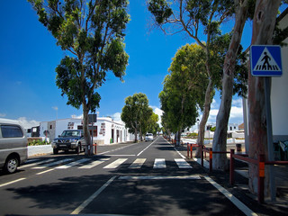 Asphalt road through the southern village with whitewashed houses. White clouds on a blue sky. Lanzarote, Canary Islands, Spain