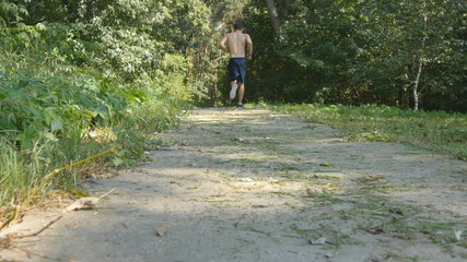 Young muscular athlete running at the forest path. Active strong man training outdoors. Fit handsome athletic male sportsmen working out. Guy training and exercising. Healthy lifestyle. Rear back view