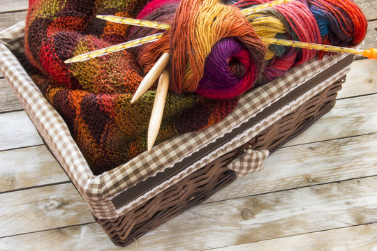 Colorful skeins of wool and wood needles in knitting basket on wooden table