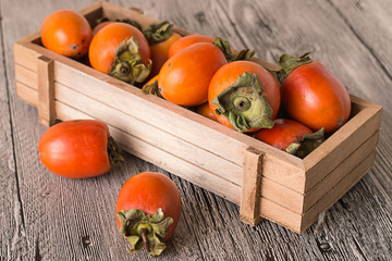 
 Persimmon in a wooden box.    Juicy ripe persimmon in a wooden box on a gray wooden background.