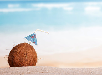 Coconut, straw and umbrella in the sand against sea.